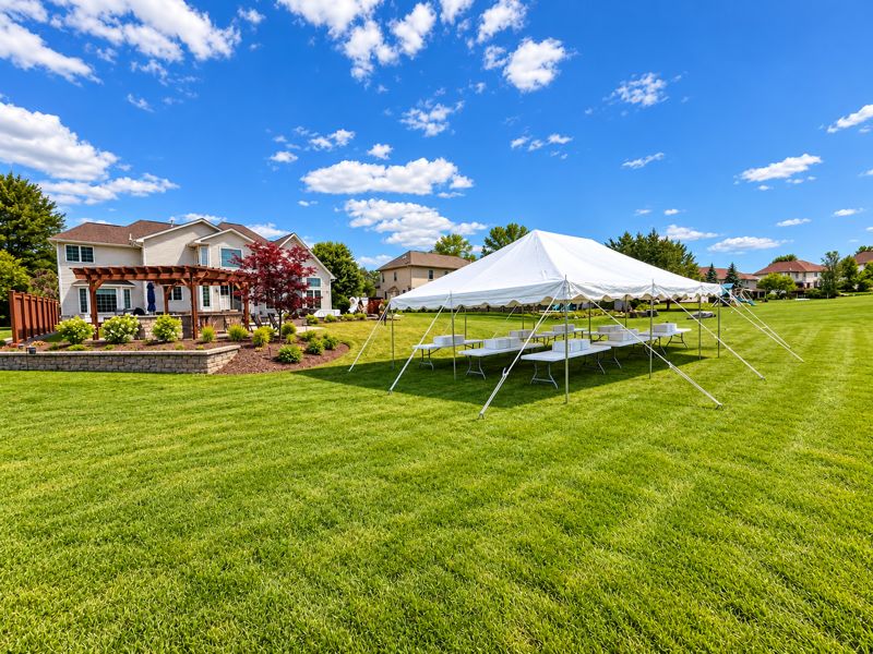 Tent with banquet tables beside a large home and patio