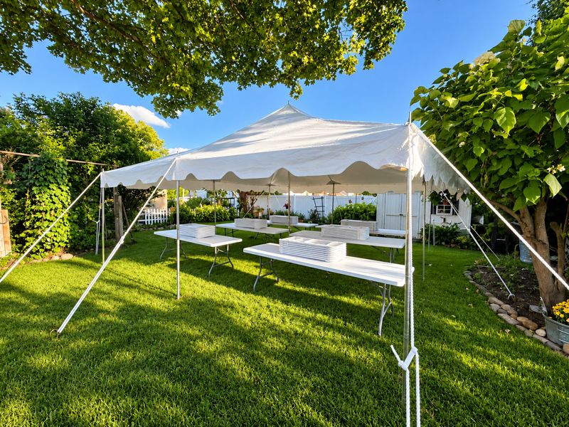 Banquet tables with stacked chairs ready under a tent in a garden backyard