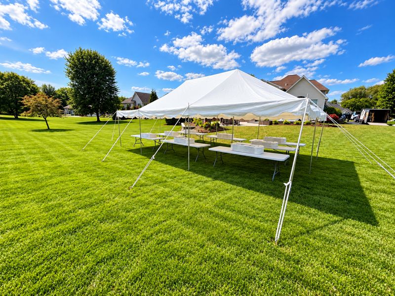 Pole tent with tables on a large open lawn under a blue sky